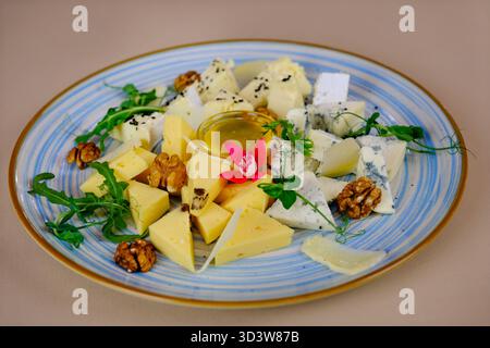 Ein wunderschön angeordneter Teller bietet verschiedene handwerkliche Käsesorten, garniert mit frischen Früchten, Nüssen und einem Honig, die Gäste zu einem Gourmet-Erlebnis einladen. Hochwertige Fotos Stockfoto