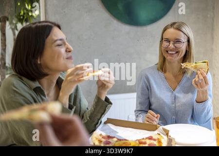 Mittagszeit. Freunde, die sich während des Mittagessens amüsieren und Pizza genießen Stockfoto