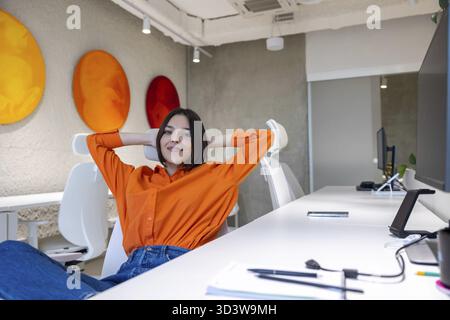 Lächelnd zufrieden, zuversichtlich schöne junge kaukasische Geschäftsarbeiterin, die allein am Schreibtisch sitzt Stockfoto