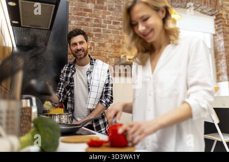 Junge glückliche Paare, die gemeinsam kochen und gesunden Salat und Pasta in ihrer Küche zubereiten Stockfoto