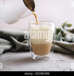 Essen, einen Kaffee mit Milch aus der Teekanne in eine Glasschale gießen Stockfoto