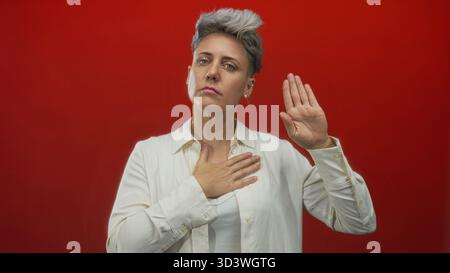Kaukasische Frau mit kurzen Haaren, Hand auf Brust legen und Handfläche im Studio heben; Engagement. Stockfoto