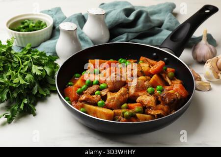 Köstlicher gekochter Eintopf in der Pfanne, Petersilie und Knoblauch auf weißem Marmortisch, Nahaufnahme Stockfoto