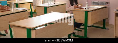 Mehrere Schüler sitzen an separaten Schreibtischen während der Unterrichtsaktivitäten, Banner. Bildung, Fernunterricht und moderne Sicherheit im akademischen Umfeld. Stockfoto
