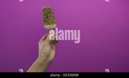 Kaukasischer Mann, der Eis mit Schokolade auf rosa Hintergrund hält, mit einer Hand isoliert in Studio-Beleuchtung für Dessert-Konzept Stockfoto