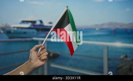Mann mit kuwaitischer Flagge am Seehafen mit sichtbarem Boot im Hintergrund unter klarem Himmel im Freien, was den kulturellen Stolz und die malerische maritime siedi hervorhebt Stockfoto