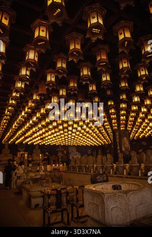 Eine leuchtende Halle mit Hunderten hängender Laternen und Reihen von Buddha-Statuen in einem traditionellen japanischen buddhistischen Tempel. Stockfoto