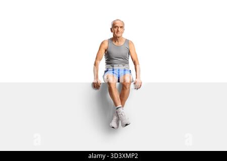 Älterer Mann in Sportbekleidung sitzt auf einer leeren Platte isoliert auf weißem Hintergrund Stockfoto