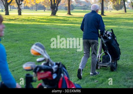 Senior-Mann, der im Herbst Golfwagen auf dem Golfplatz schiebt, einen aktiven Lebensstil und sportliche Freizeit genießt Stockfoto
