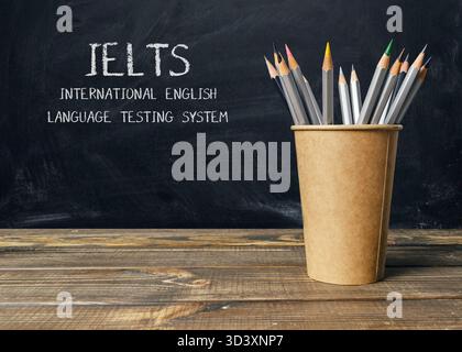 Holztisch mit einer Tasse Bleistifte und einer Tafel mit dem Wort IELTS Stockfoto