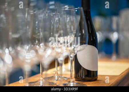 Weinflasche mit leerem Etikett auf Holzbar mit vielen Gläsern Stockfoto