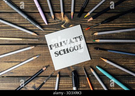 Verschiedene Schreibwaren wie Stifte und Bleistifte sind kreativ um eine Notiz angeordnet, die Privatschule liest, und gegen einen rustikalen Holzrücken gesetzt Stockfoto