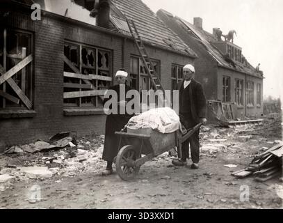 Nach dem Neede-Zyklon vom 1. Juni 1927 arbeiten ein Mann und eine Frau, beide verletzt, hart daran, ihre Häuser wieder aufzubauen. Das Foto zeigt sie mit geretteten Gegenständen in einer Schubkarre. Stockfoto