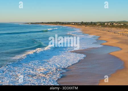 Strand in der Nähe von Kap Trafalgar, Costa de la Luz, Spanien, Andalusien. Sonnenuntergangsszene mit Wellen und Surfern im Meer. Stockfoto