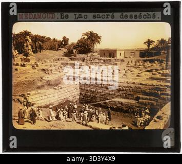 Dieses Glasdiapositiv aus der Zeit um 1924-1932 zeigt Arbeiter, die im geleerten Heiligen See von Medamud-Tempel von Montu stehen. Das Bild spiegelt die Auswirkungen der Ausgrabungsaktivitäten wider. Stockfoto