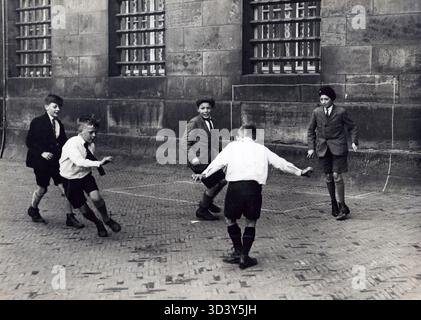 Während der Olympischen Spiele 1928 in Amsterdam spielen Kinder weiterhin Fußball auf der Straße vor dem Königspalast. Auf dem Bürgersteig wurde ein Tor markiert, während sie die Sommerpause genießen. Stockfoto