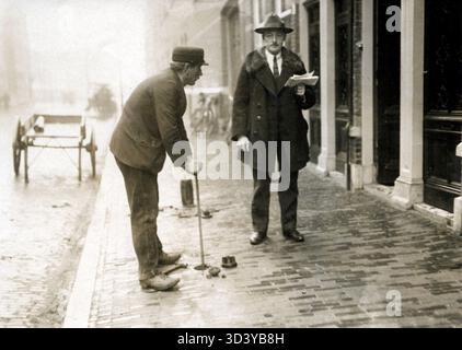 1924, während eines Wasserstreits in den Haag, geht ein gut gekleideter Mann, möglicherweise ein Beamter, die Straße hinunter und hält Papiere, während ein Arbeiter gesehen wird, wie er eine Stange in den Boden wirft. Niederlande, Fotoserie. Stockfoto