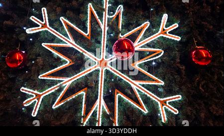 Große glühende Schneeflocke und rote Glaskugeln in Nahaufnahme auf dem Weihnachtsbaum, helle und schöne Neujahrs- und Weihnachtsdekoration Stockfoto