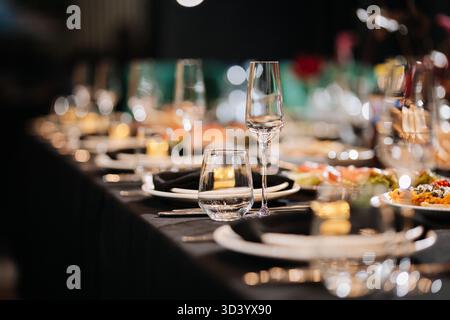 Nahaufnahme eines eleganten Banketttisches mit Gläsern und schwarzen Servietten in sanftem Bokeh-Licht Stockfoto