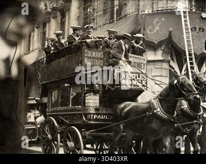 Dieses Foto aus dem Jahr 1911 zeigt einen Omnibus, der von zwei Pferden gezogen wird. Junge Männer in Strohhüten sitzen oben, mit Werbeschildern, darunter für Colman’s Senf, die an der Straßenbahn hängen. Stockfoto