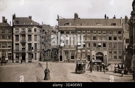 Ein Blick auf die Häuser am Damm in Amsterdam, darunter das Van Gend & Loos Gebäude (1886 abgerissen), an dem zwei Pferdekutschen vorbeifahren. Das Bild zeigt auch das Schild „Horlogerie Suisse“ an der Ecke Nieuwendijk. Um 1877. Stockfoto
