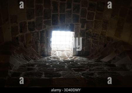 Atmosphärischer, flacher Blick in die historische Festung Koules. Sonnenlicht strömt durch ein kleines, vergittertes Fenster in der dunklen Steinmauer. Stockfoto