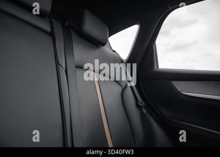 Rücksitz im Auto – niedriger Kamerawinkel, Weitwinkelansicht. Innenraum für SUV oder Wagen mit schwarzen Ledersitzen mit perforierten Einsätzen und beigefarbenem Streifen. Stockfoto