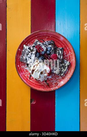 Schokoladendessert mit Erdbeeren, Beeren und Schlagsahne auf einem bunten Holztisch. Ansicht von oben Stockfoto