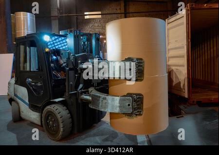 Große Gabelstapler, die Papierrollen in einem belebten Papierfabriklager während des Abendbetriebs handhaben Stockfoto