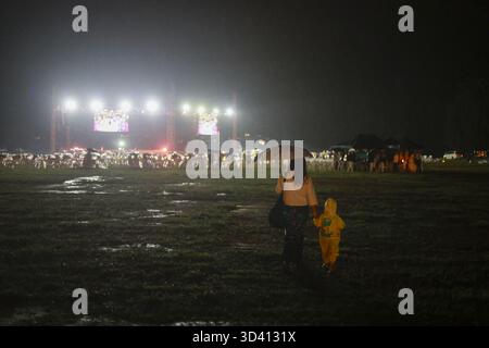 Schützende Mutter und ihr Kind gehen bei einem Musikfestival nachts durch Regen und Schlamm. Diese Familie benutzt einen Regenschirm, um die Konzertbühne zu verlassen Stockfoto