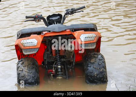 Kraftvolles oranges Geländefahrzeug, das nach einem Sturm in tiefem matschigem Hochwasser stecken geblieben ist. Verlassenes Quad steht vor einem herausfordernden Problem, das in schmutzige, trübe R eingetaucht ist Stockfoto