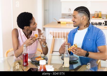 Mit dem Smartphone können Sie sich mit verschiedenen Freunden unterhalten, die Sandwiches am Glastisch in der modernen Küche essen Stockfoto