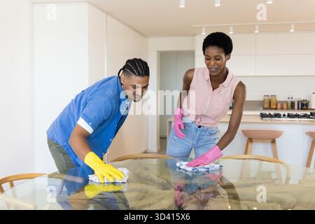Verschiedene Mitbewohner putzen Glastisch in moderner Küche, mit bunten Gummihandschuhen Stockfoto