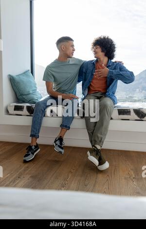 Verschiedene männliche Freunde, die auf gepolstertem Fenstersitz in einer hellen Lounge mit Blick auf die Berge sitzen Stockfoto