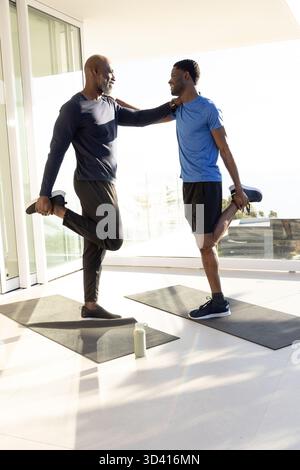 Afroamerikanische Freunde dehnen sich, während sie im Heimstudio auf einem Bein balancieren, mit Yogamatten Stockfoto