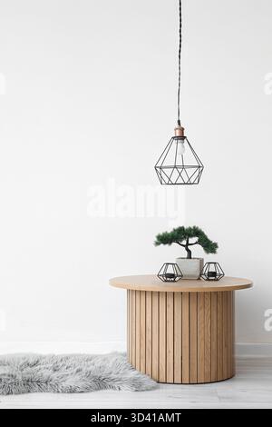 Couchtisch aus Holz mit Bonsaibaum und Kerzenständer in der Nähe der weißen Wand Stockfoto