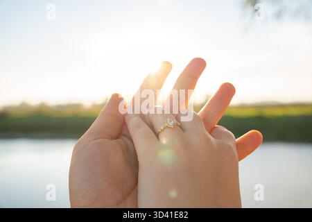 Ring-on-Finger-Konzept symbolisiert Liebesantrag Ehe und Romantik in der Natur bei Sonnenuntergang. Sonnendurchflutete Hand zeigt einen goldenen Verlobungsring Stockfoto