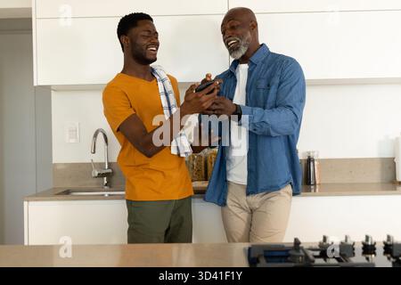 Afroamerikaner Vater und Sohn mit schwarzer Pfeffermühle an der Küchentheke mit Handtuch zermahlen Stockfoto