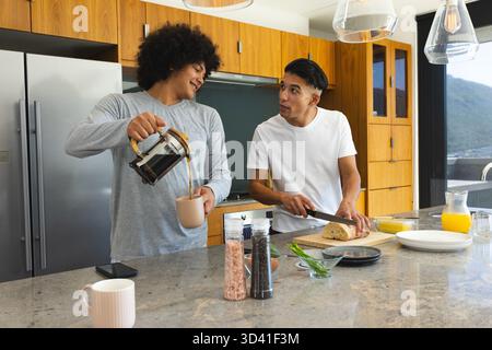 Verschiedene männliche Freunde bereiten Frühstück in moderner Küche zu, mit französischer Presse und frischem Brot Stockfoto