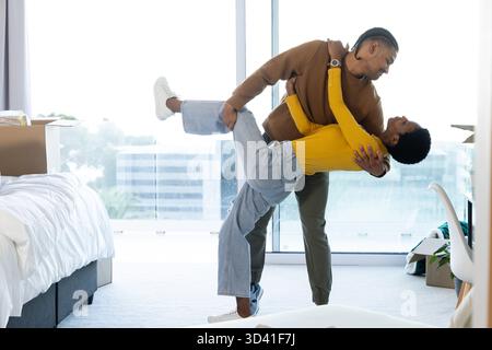 Tanzendes, vielseitiges Paar, das ein verspieltes Bad in einem Apartment mit Boxen und raumhohen Fenstern spielt Stockfoto
