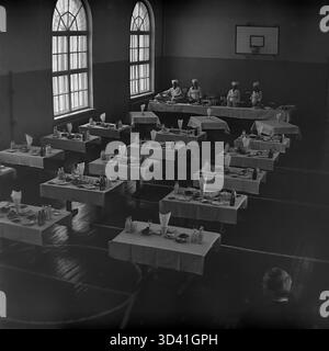 Ein Archivfoto aus dem Jahr 1984 zeigt die Kantine für Delegierte im Artyom House of Culture (DK) in Sloviansk, Ukrainische SSR. Diese hohe Aussicht zeigt das Fitnessstudio mit einem Basketballkorb und markiertem Boden, das in einen Speisesaal umgewandelt wurde. Die Tische sind mit weißen Tischdecken, Mahlzeiten und Milchflaschen aus Glas besetzt. Vier Köche stehen in Uniform an der Buffetlinie. Das ist das Catering für eine offizielle sowjetische Veranstaltung. Dies ist ein Moment des Alltags im friedlichen Donbass vor dem Krieg. Stockfoto