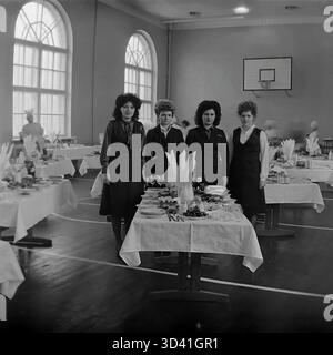 Ein Archivfoto aus dem Jahr 1984 zeigt vier Delegierte auf einer Bezirks- und Stadtkonferenz in Sloviansk, ukrainische SSR. Die Frauen posieren für ein Porträt hinter ihrem Tisch während einer Mittagspause. Die Kantine wurde zeitweise im Turnsaal des Kulturhauses Artyom (DK) eingerichtet, was an den Bogenfenstern und dem Basketballkorb zu erkennen ist. Der Tisch ist mit Tellern mit Speisen, Obst und Getränken gedeckt. Dies fängt die Atmosphäre eines offiziellen sowjetischen Ereignisses ein. Dies ist ein Moment des Alltags im friedlichen Donbass vor dem Krieg. Stockfoto