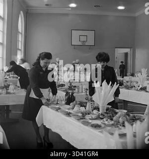 Ein Archivfoto aus dem Jahr 1984 zeigt Kellnerinnen, die sich auf ein Bankett im Artyom House of Culture (DK) in Sloviansk, ukrainische SSR, vorbereiten. Die Konferenzkantine wurde in der Turnhalle eingerichtet, wie der Basketballkorb zeigt. Die Kellner in dunklen Kleidern und weißen Schürzen haben Tische mit Tellern, Obst und Glasmilchflaschen gedeckt. Im Hintergrund stehen Köche in Kochmützen an der Buffetzeile. Das ist das Catering für eine offizielle sowjetische Veranstaltung. Dies ist ein Moment des Alltags im friedlichen Donbass vor dem Krieg. Stockfoto