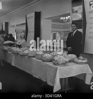 Ein Archivfoto aus dem Jahr 1984 zeigt das Buffet für Delegierte im Artyom House of Culture (DK) in Sloviansk, ukrainische SSR. Ein männlicher Delegierter im Anzug posiert an einem langen Tisch im Foyer. Der Tisch ist voll mit Korbkörben mit Gebäck, wahrscheinlich Baisons. Im Hintergrund stehen Propagandaständer an der Wand, und ein Mitarbeiter in Uniform dient den Gästen. Dies fängt die Atmosphäre einer offiziellen sowjetischen Konferenz ein. Dies zeigt den Alltag im friedlichen Donbass vor dem Krieg. Stockfoto