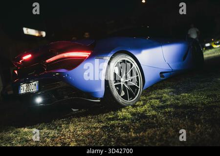 Mailand, italien 28. oktober 2025: Blaue mclaren 720er-Jahre-Rückansicht bei Nacht, auf Gras geparkt mit leuchtenden Rückleuchten, die den eleganten, leistungsstarken Luxus hervorheben Stockfoto