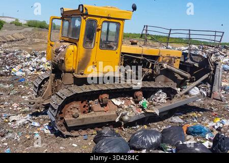 Ein Bulldozer entfernt Müllhaufen in einem Mülleimer. Arbeiten Sie mit dem Planierschild auf einer Deponie. Müllkippe, Draufsicht auf den Müll. Deponie. Stockfoto