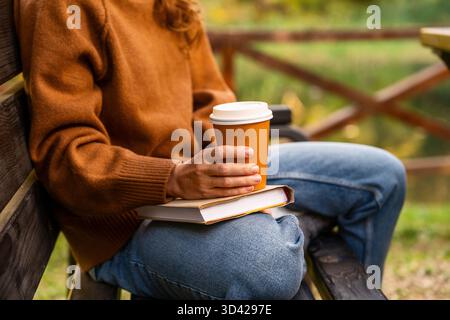 Frau, die eine Tasse Kaffee zum Mitnehmen hält, während sie sich draußen im Herbstpark entspannt Stockfoto