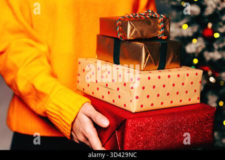 Stapel Weihnachtsgeschenkboxen in den Händen einer Frau, die einen warmen gelben Pullover trägt. Stockfoto