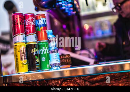 Mailand, italien 27. oktober 2025: Verschiedene gebrandete Soda-Dosen und eine Trinkflasche aus Plastik stehen auf einer neonbeleuchteten Bar, bereit für durstigen Kunden Stockfoto