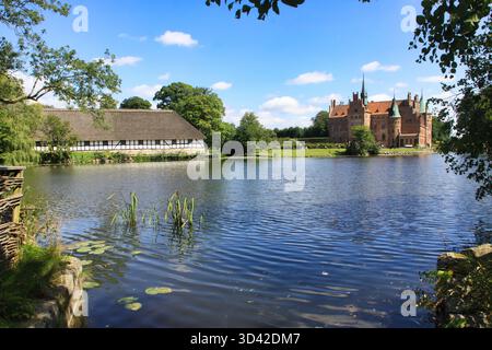 Egeskov Slot, Fünen, Dänemark, 08/14/2012 Beschreibung: Blick auf Schloss Egeskov, Wassergraben und traditionelles Strohdachgebäude, Dänemark Stockfoto